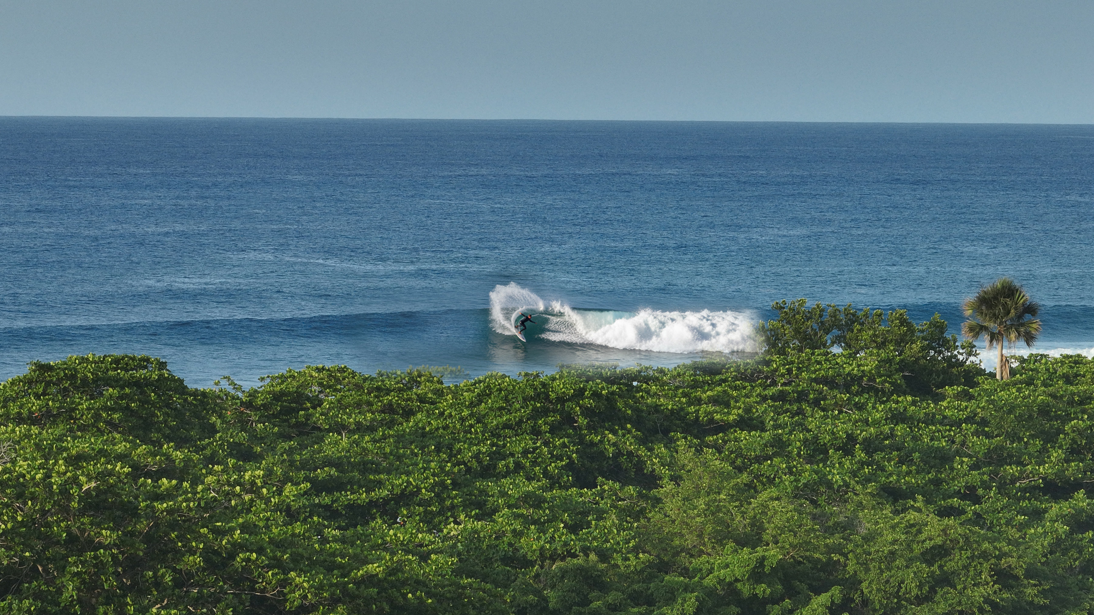 A surfer in the barrel on the wave in front of the ATABAY land